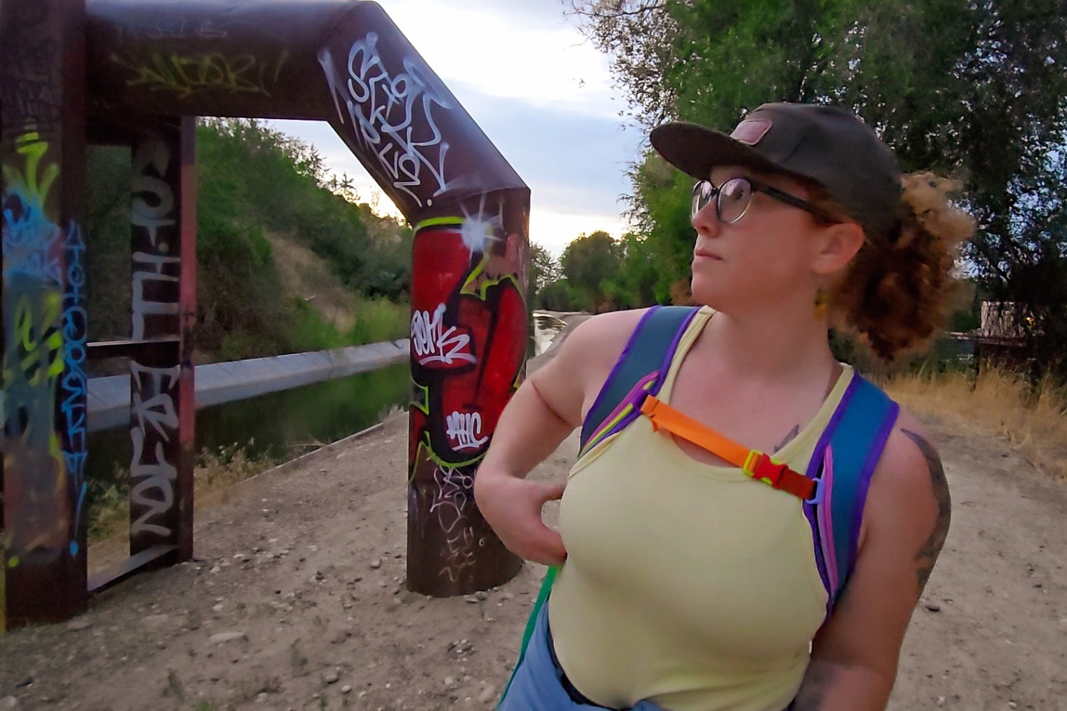 A person wearing a colorful Cotopaxi daypack walks toward the camera and displays the fit of the sternum strap.