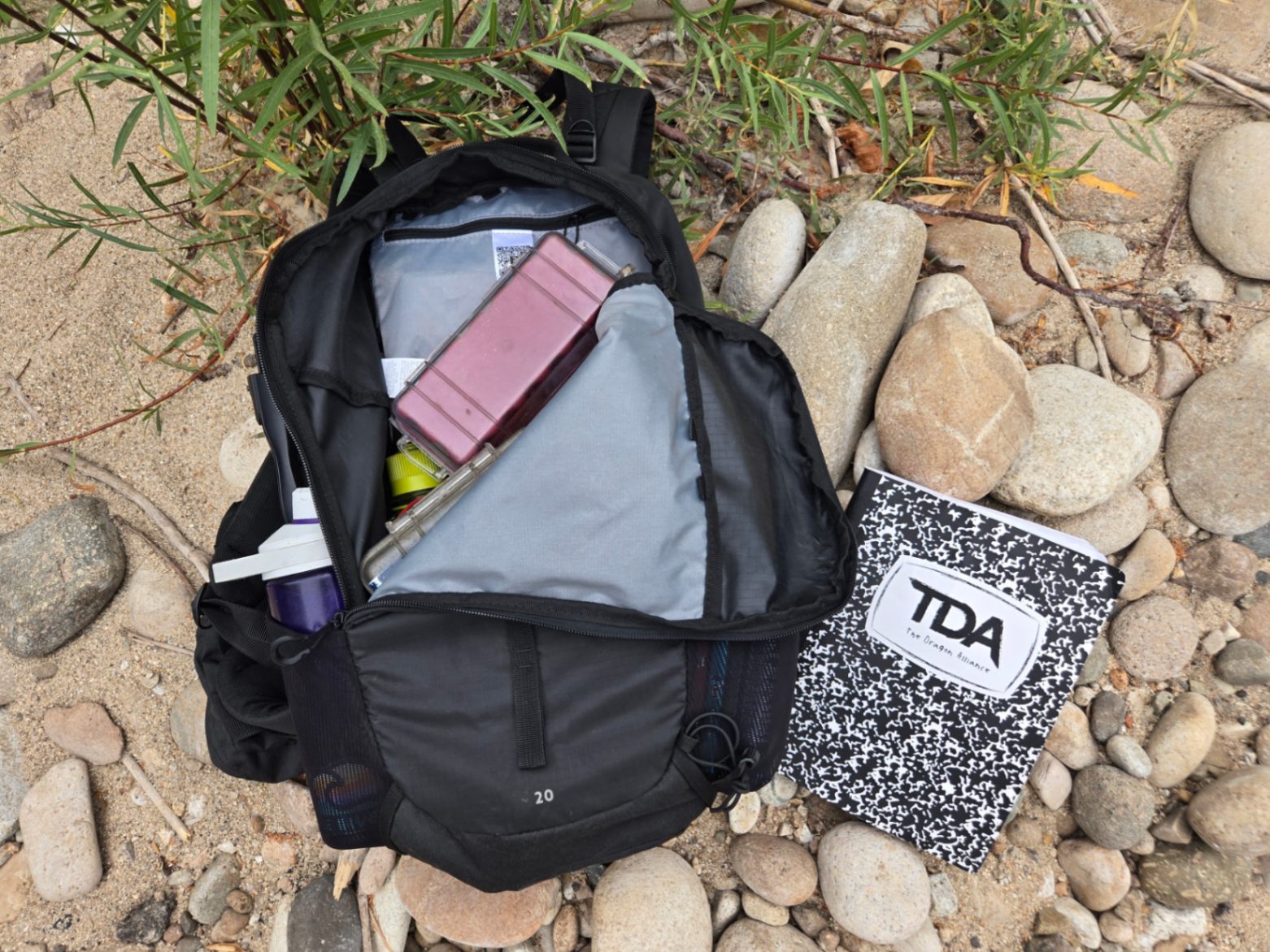 A black Decathlon Quechua MH100 20L pack lies on the ground with the zipper open, showing the internal contents.