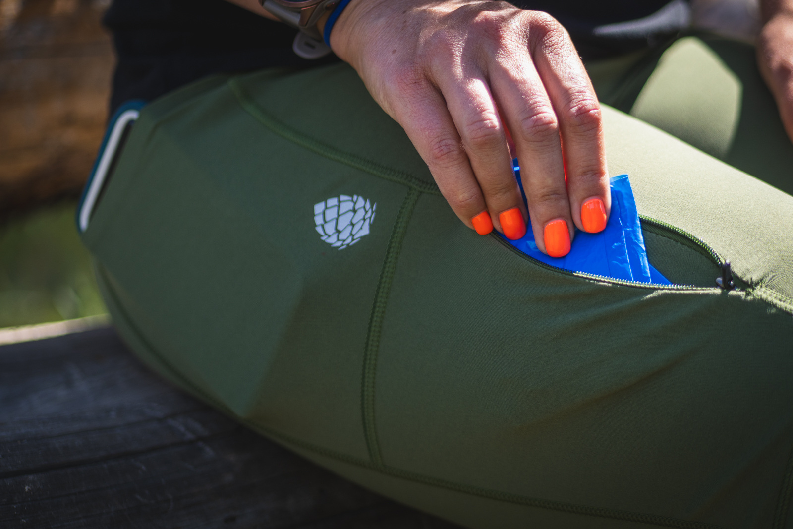 Women in green hiking leggings, pulling a blue bag out of her zipper pocket.