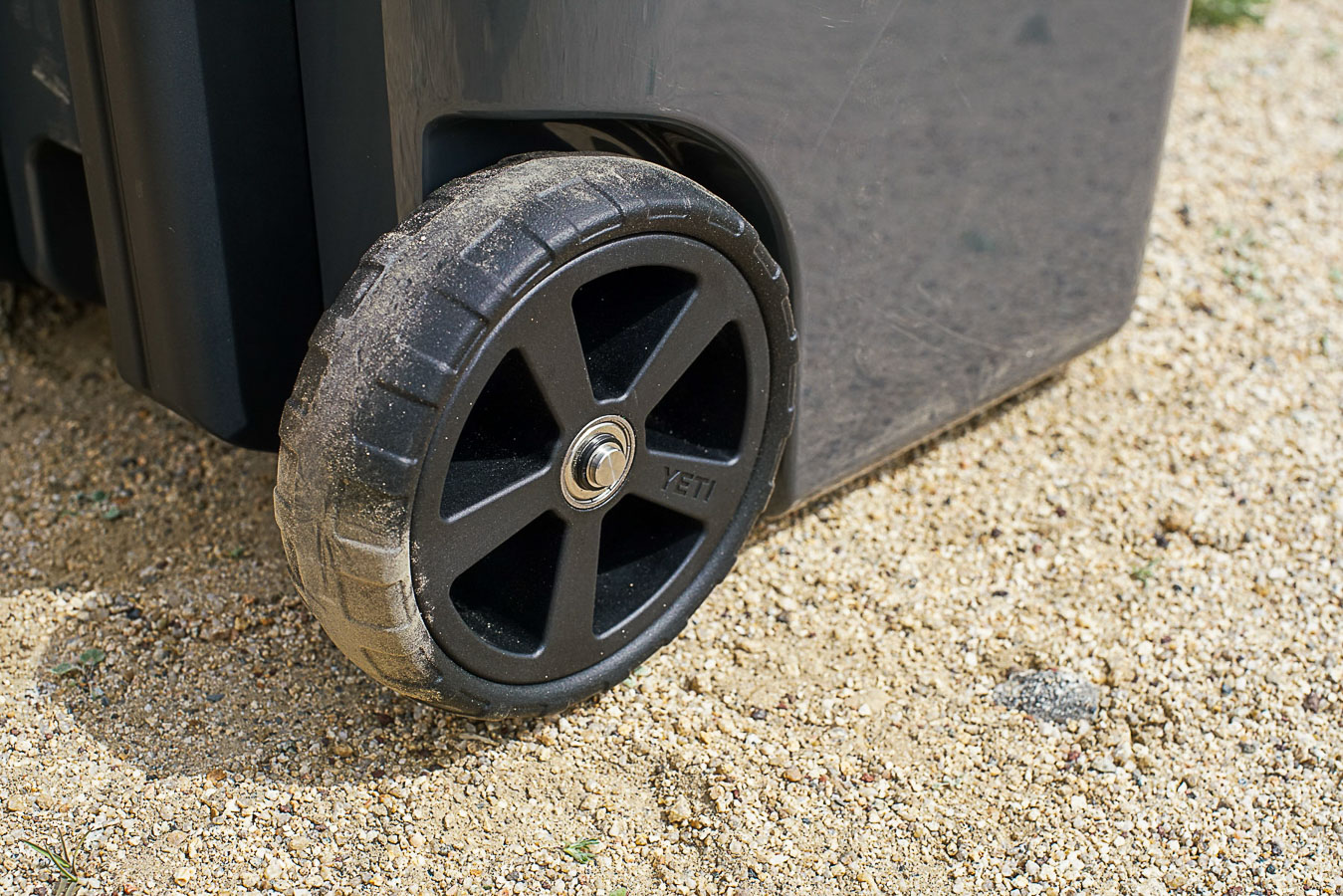 A close up of a single wheel on the YETI Roadie 48 cooler on a gravelly terrain. The wheel is dusty.
