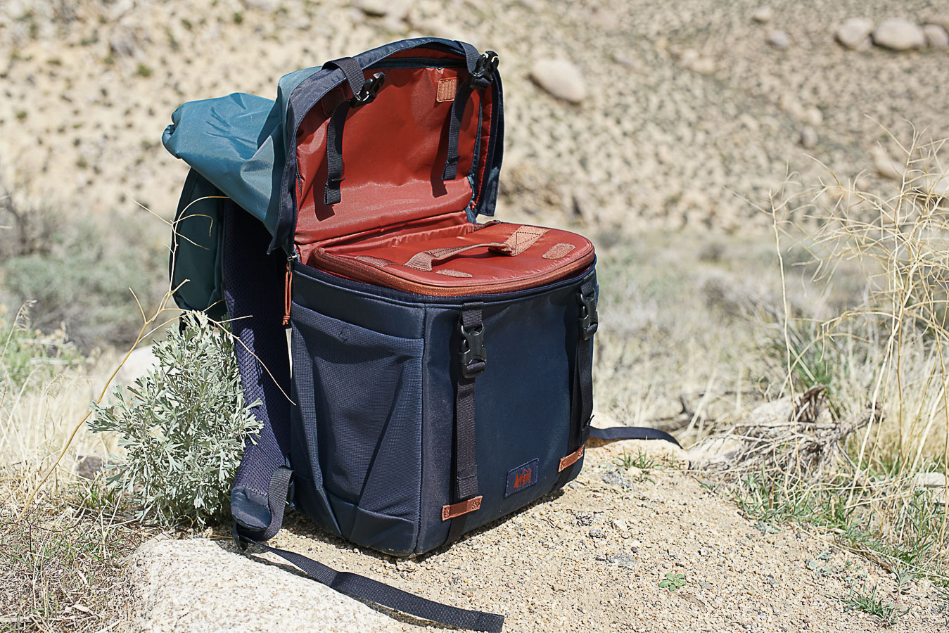 The REI Cool Trail Split Pack sits on the ground. The pack is zipped open from the middle and the cooler insert is visible.