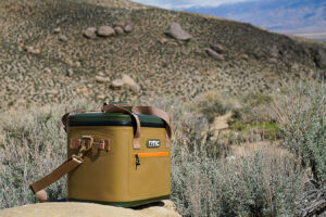 The RTIC Soft Pack cooler sits on a rock with sage brush and boulders in the background.