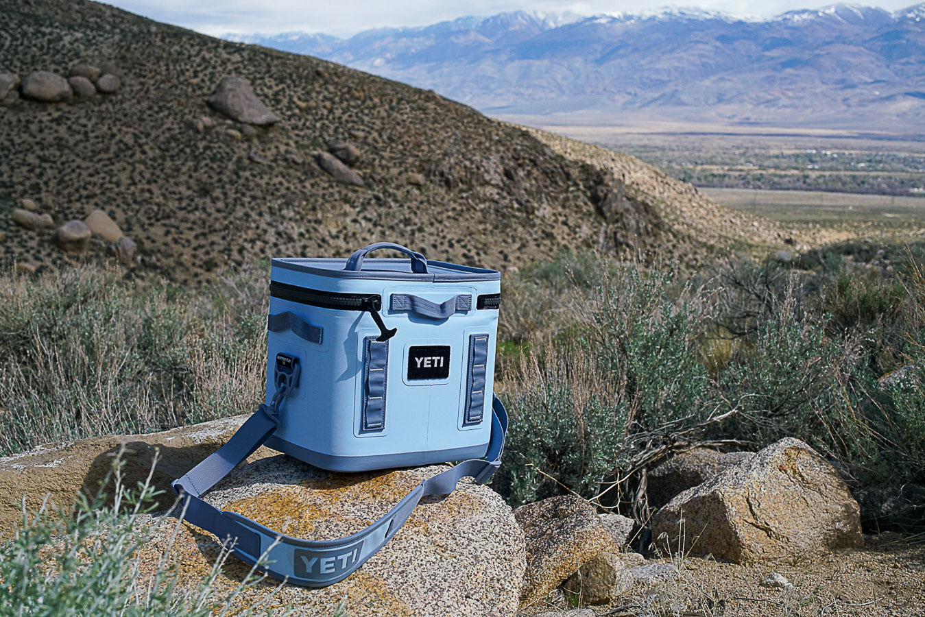 The YETI Hopper Flip 12 sits on a rock with sage brush and boulders in the background.