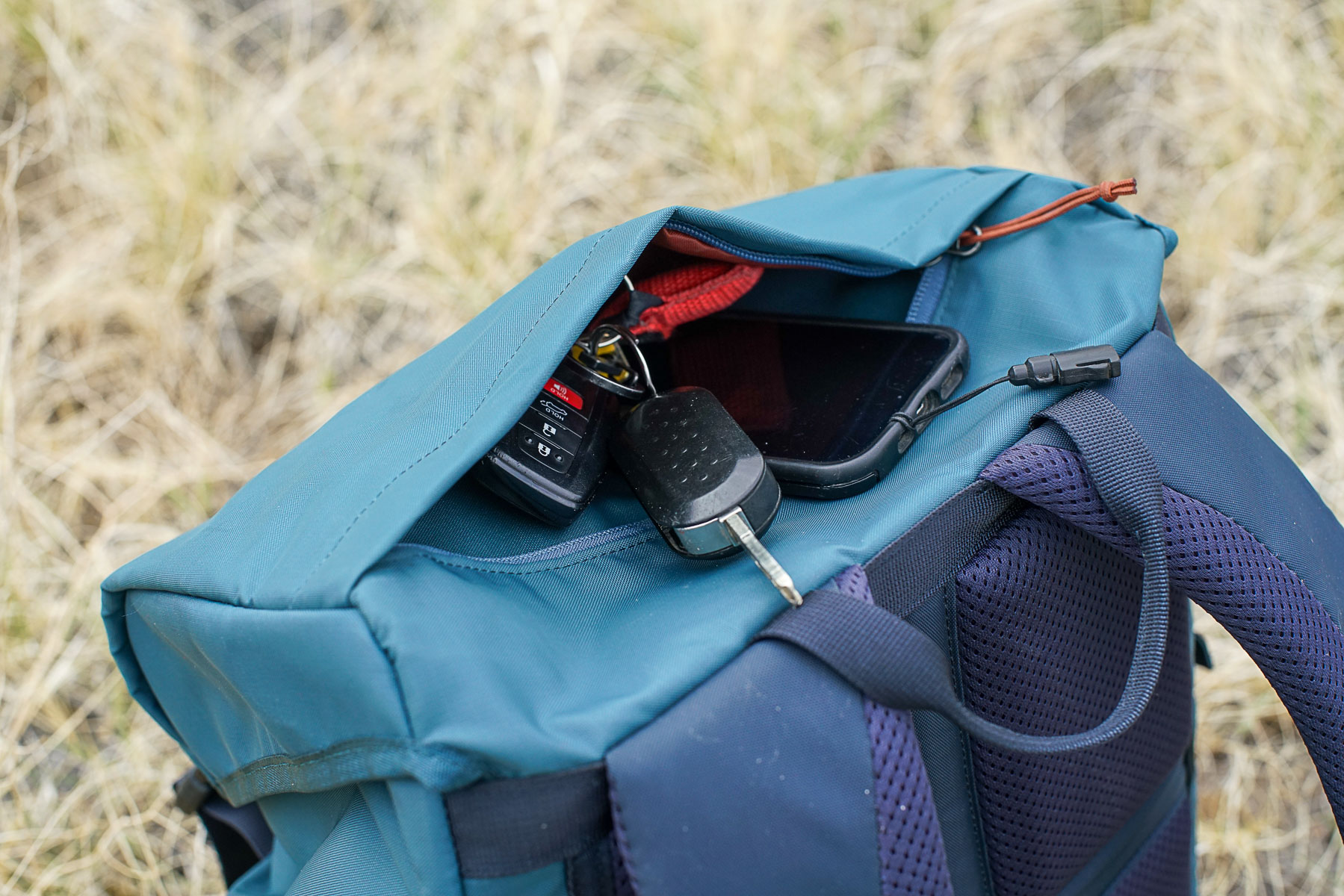 A close up of the top lid pocket on the REI Cool Trail Split Pack. Some car keys and a phone stick out of the partially unzipped pocket.
