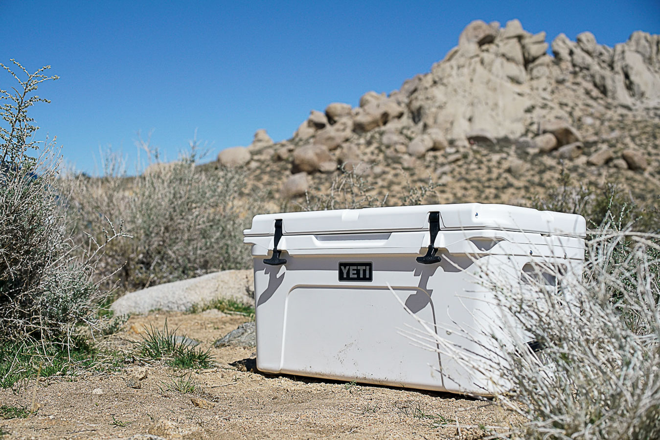 The YETI Tundra 65 sits on the ground with boulders in the background.