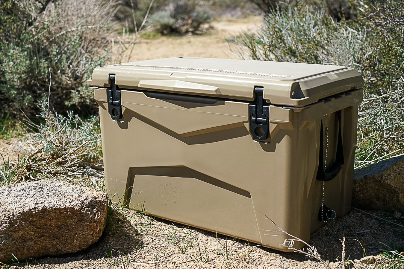 The XSpec 60QT cooler sits on the ground beside a small rock and sage brush.
