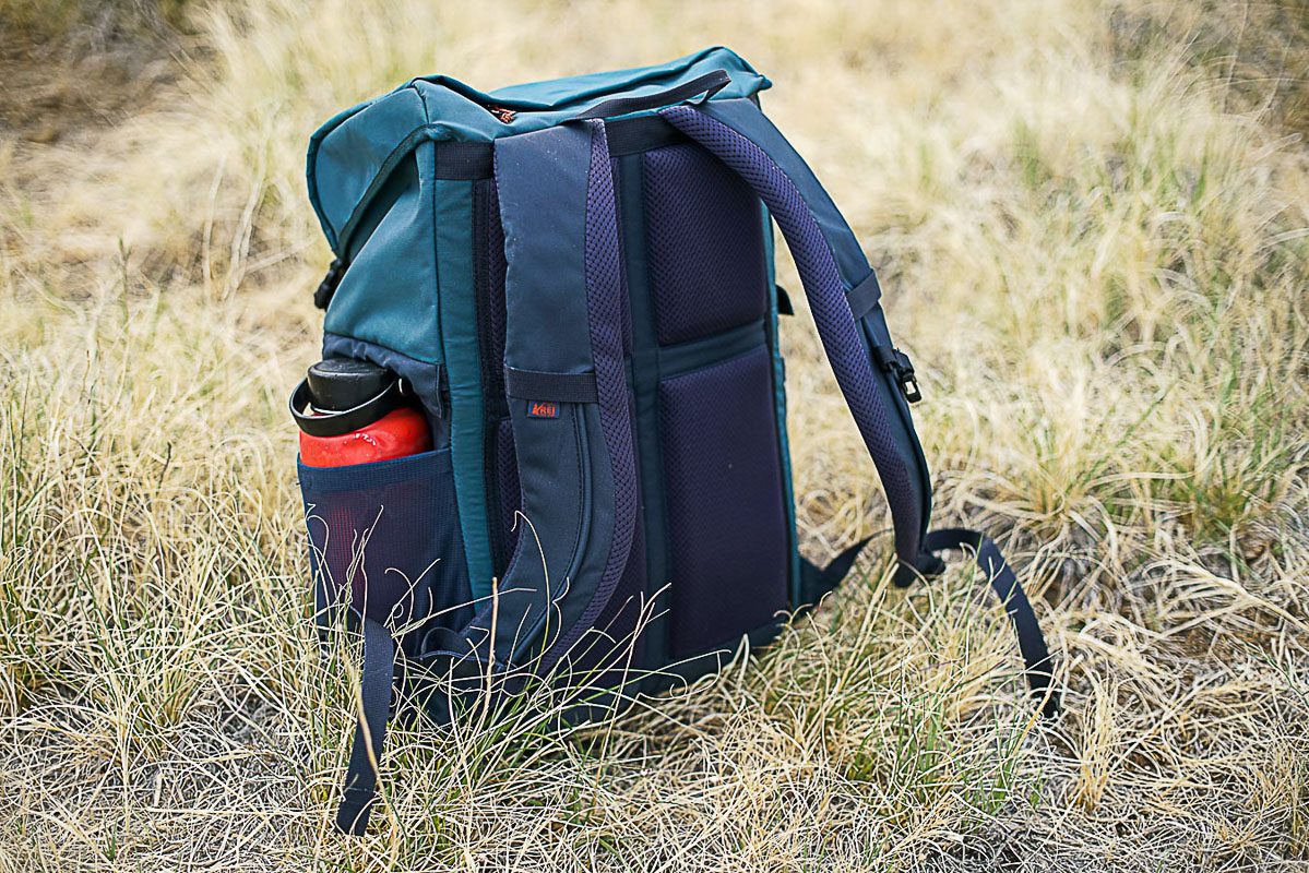 The REI Cool Trail Split Pack sits upright on grassy ground.