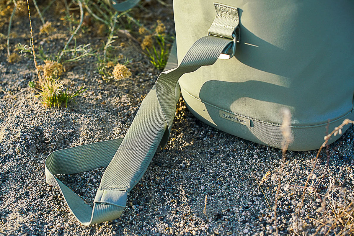A close up of the shoulder strap on the Hydro Flask Carry Out 20L. The cooler and strap sit on the ground.