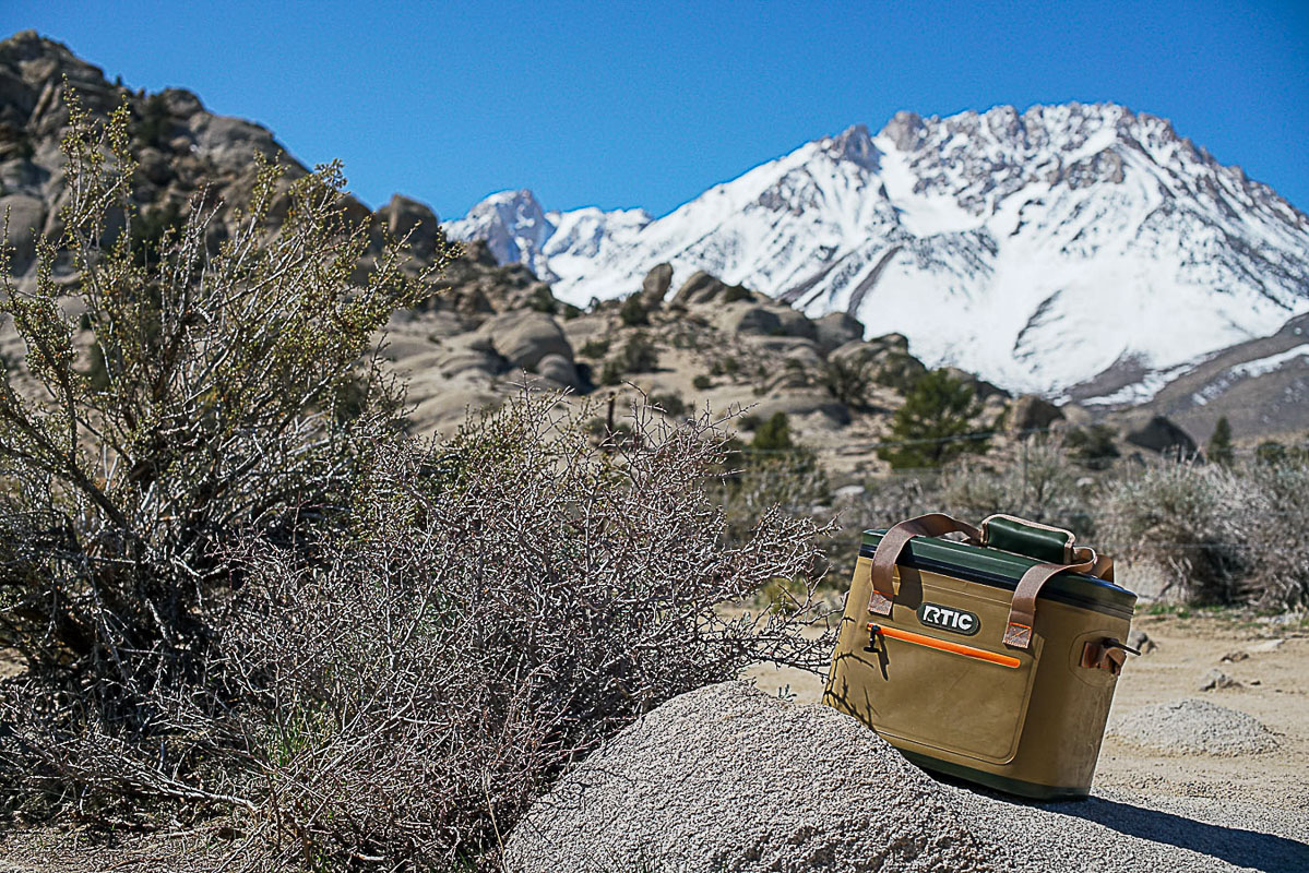 The RTIC Soft Pack leans on top of a rock with boulders and a mountain in the distance.