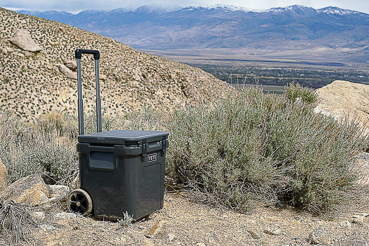 The YETI Roadie 48 cooler sits on the ground with mountains in the background.