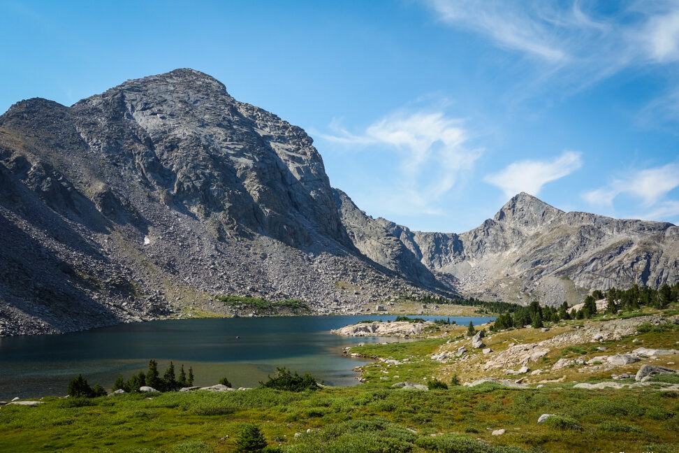 a large blue and green lake below a massive granite peak