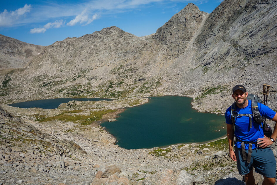 backpacker posing on a pass above two lakes in a rocky granite area