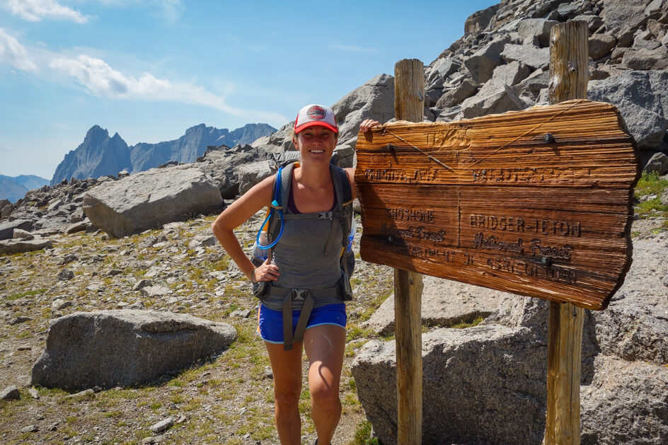 a woman posing next to a sign on a trail that says texas pass in the bridger teton wilderness