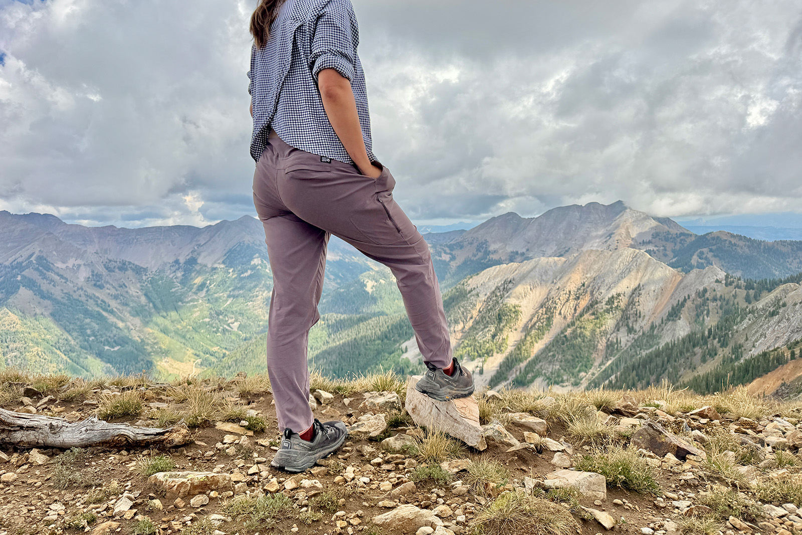 The Dynama pants are featured as a person is standing on a mountain looking at a view of other mountains in the distance.