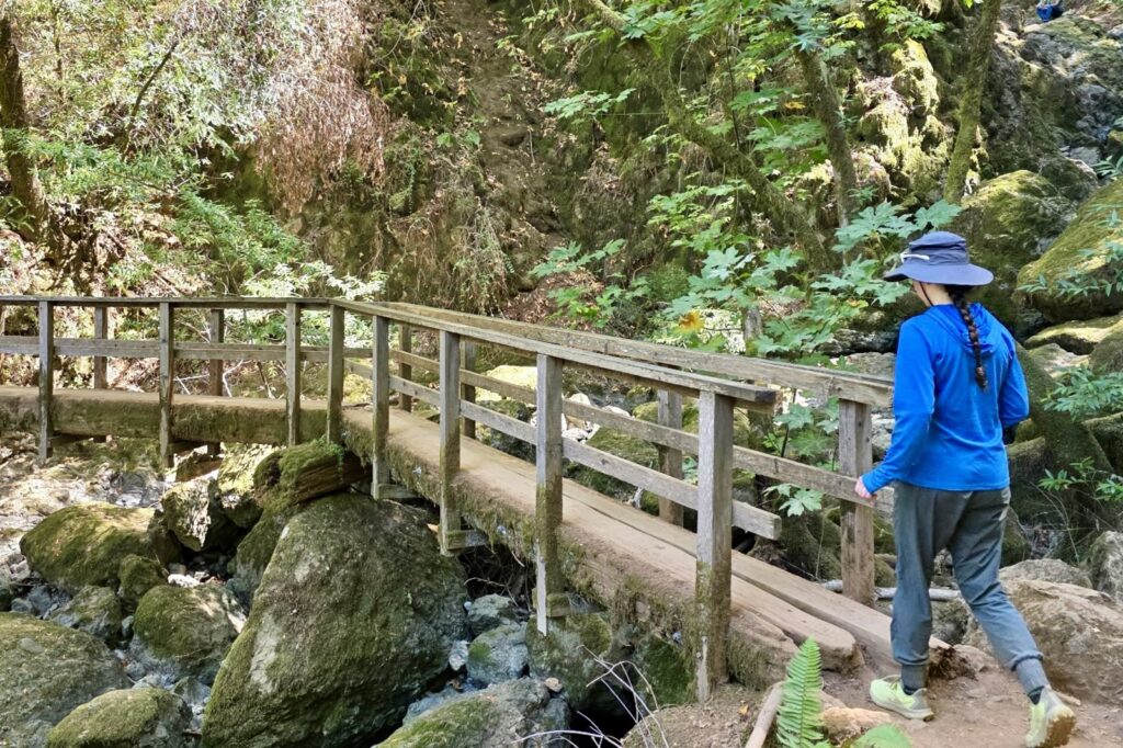 A woman walks across a bridge wearing her sun hat.