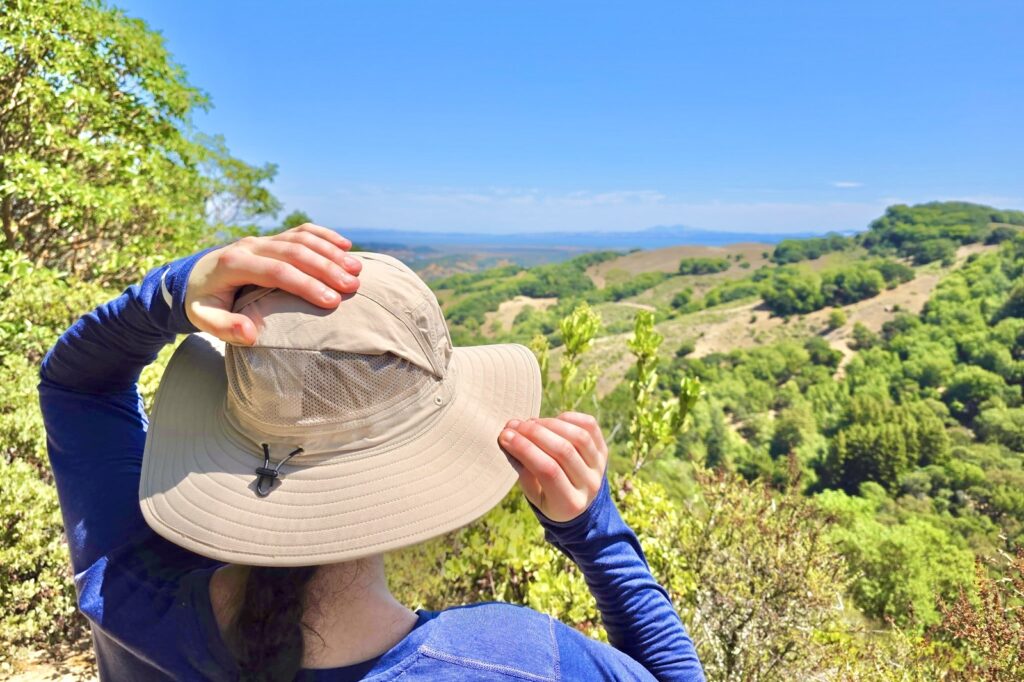 A woman pulls up the mesh panels on her sun hats while stopping at an overlook on the trail.