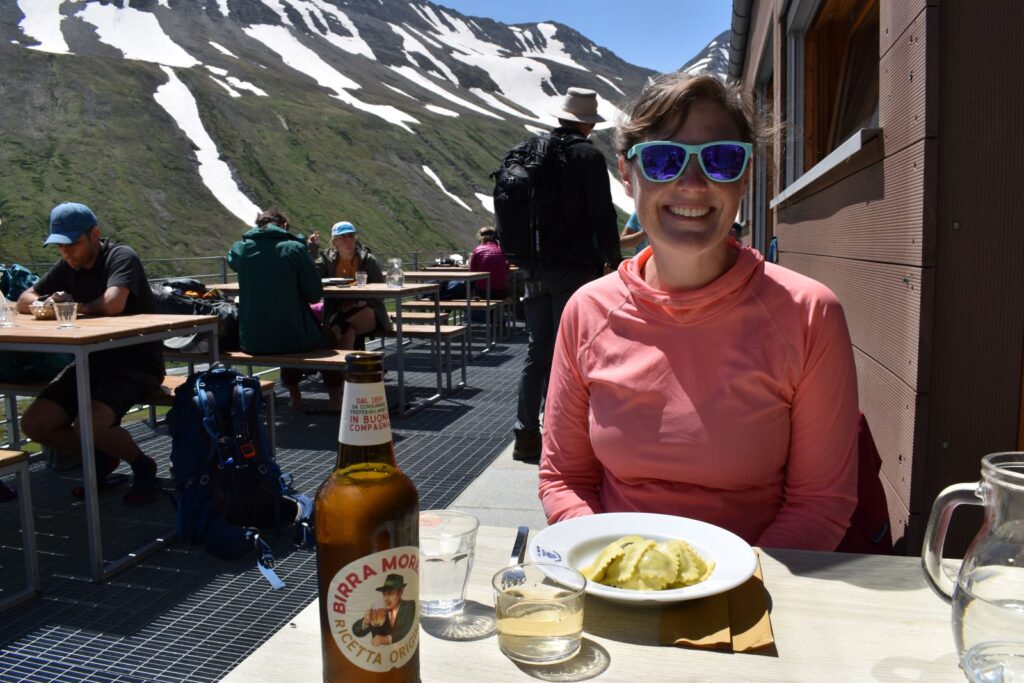 A female hiker smiles while eating homemade ravioli at an Italian refuge
