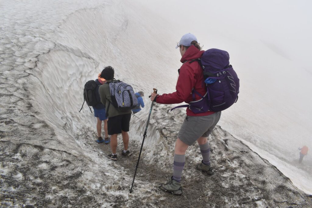 Hikers in regular shoes hold up a hiker in microspikes while descending from the Swiss border