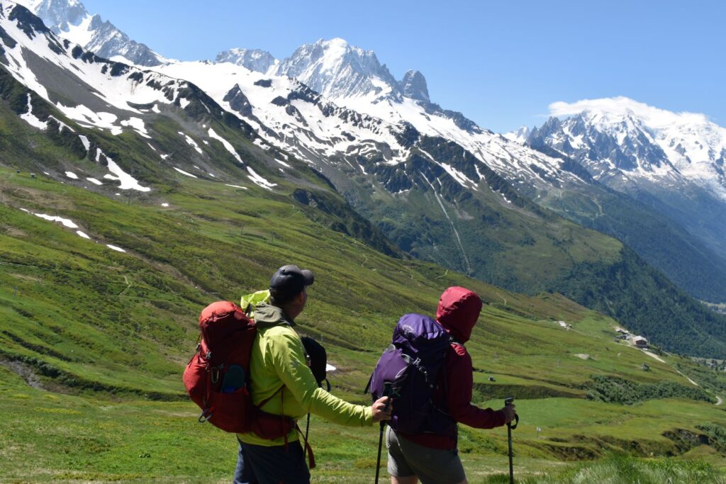 Two hikes look over a green ski area to see snowy Mont Blanc in the distance