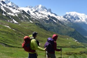 Two hikes look over a green ski area to see snowy Mont Blanc in the distance