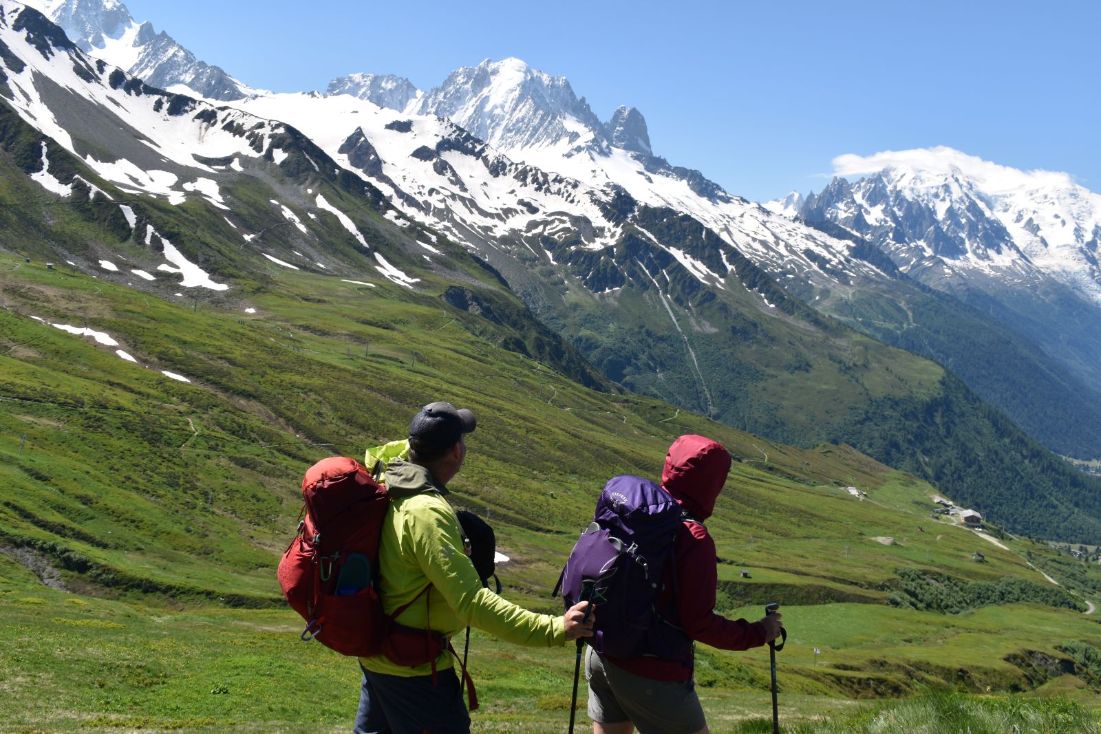 Two hikes look over a green ski area to see snowy Mont Blanc in the distance