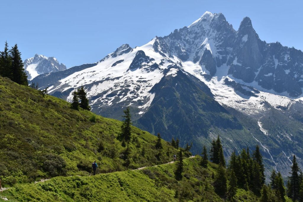 Two people hike across a green hillside in the Alps before turning left onto the next switchback