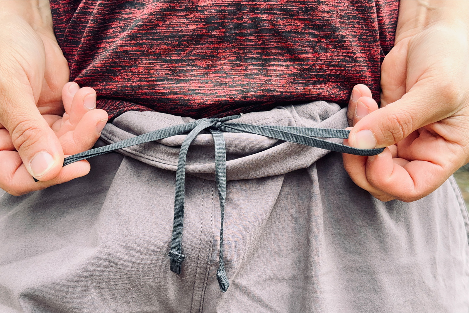 Close up shot of two hands tying a bow with the waist tie of the Mountain Hardware Dynama 2/Ankle pants.