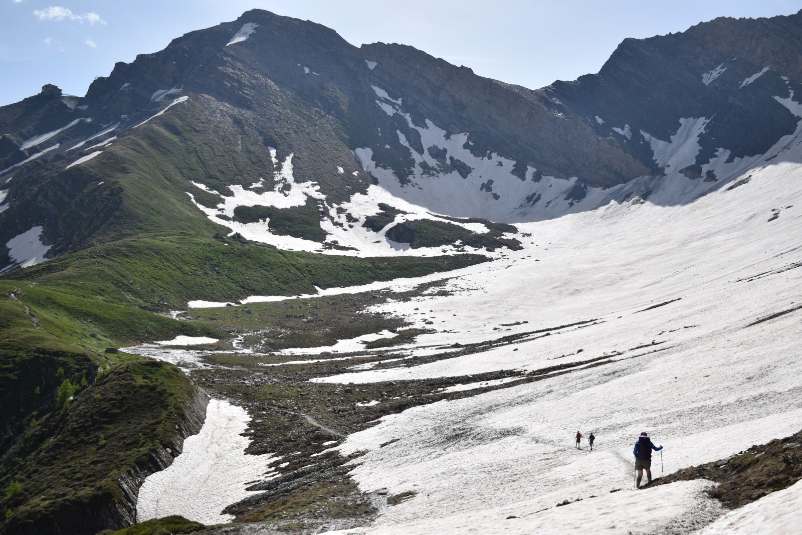 A few hikers spread out over a snowfield on a steeper plan of the TMB in France