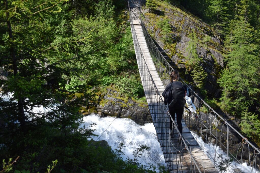 A female hiker crosses a temporary suspension bridge over a whitewater stream on Stage 1 on the TMB