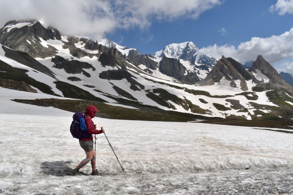 A female hiker walks across a snowfield in the Italian alps while using her trekking poles for traction and balance