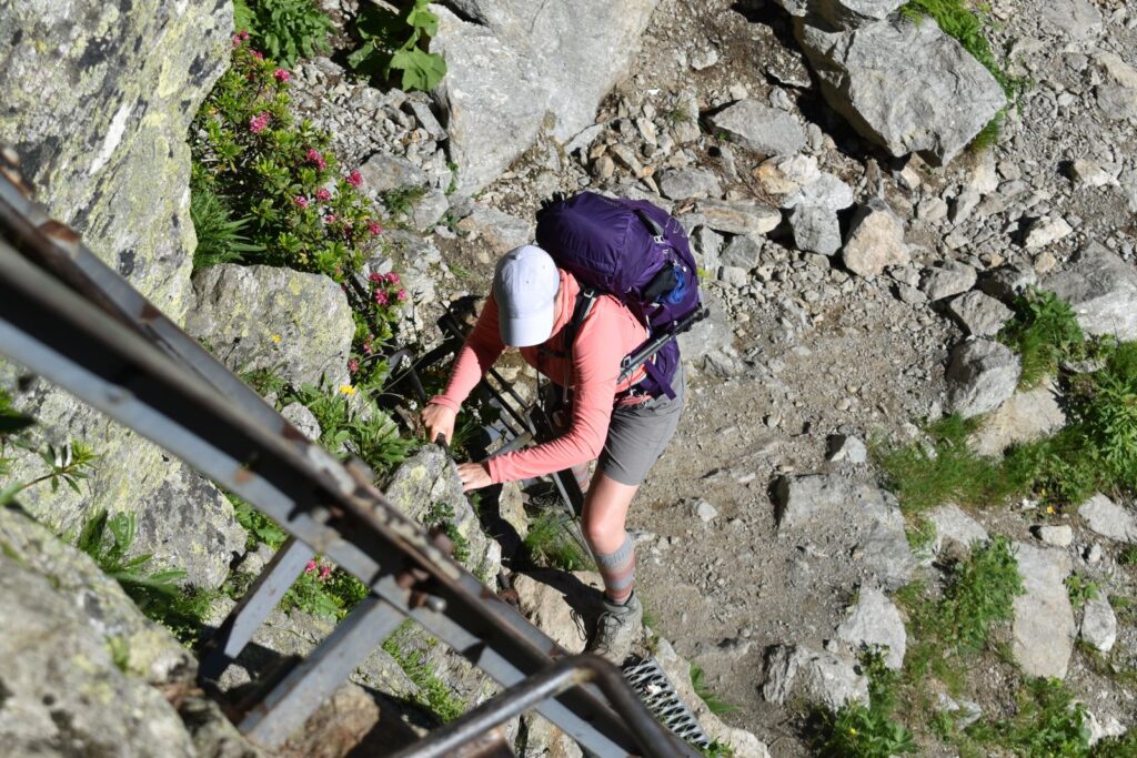 A female hiker in a pink fleece top switches from one ladder to another on the TMB