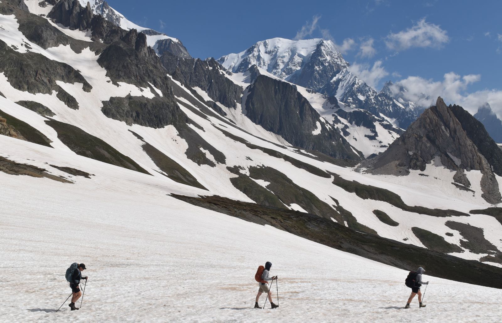 Three hikers walk across a snowfield a few miles into Italy on the Tour du Mont Blanc