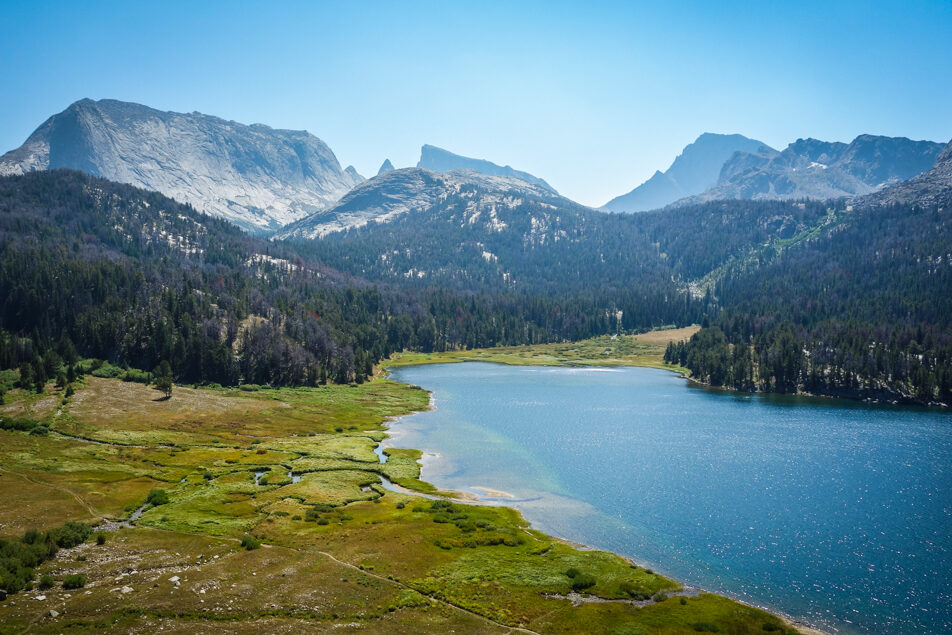 a big lake with sandy shores sits in front of large granit peaks in the distance make up part of the wind river range