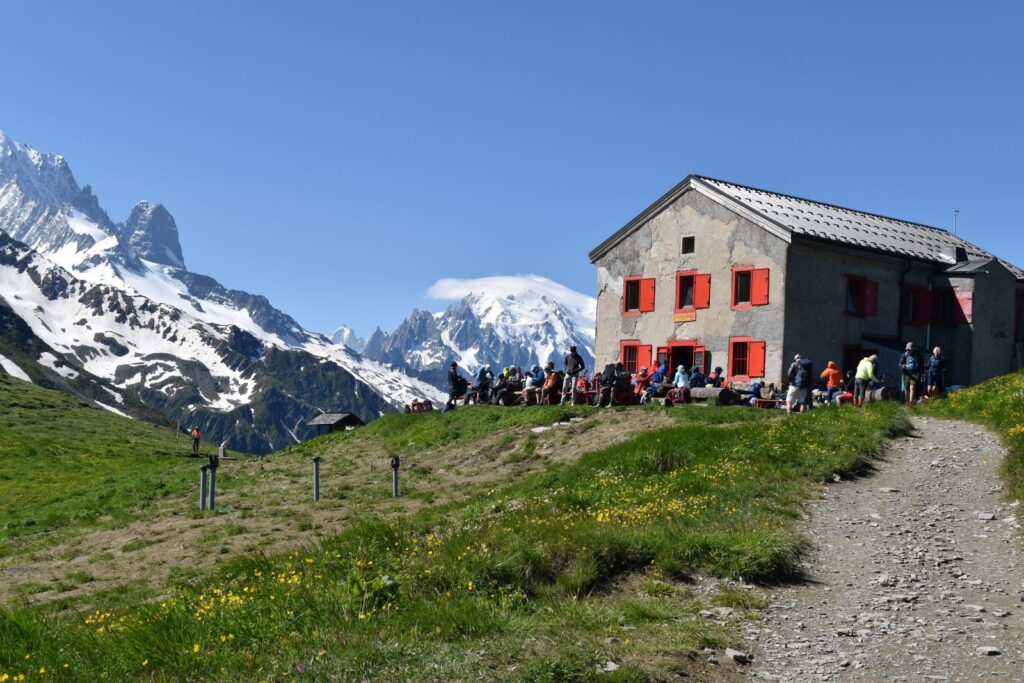 A square stone building with red shutters sits on a scenic mountain pass on the border of Switzerland and Italy