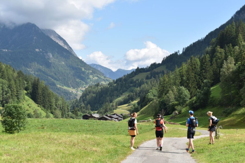 5 trail runners finish a rest stop in a green valley in the Swiss Alps