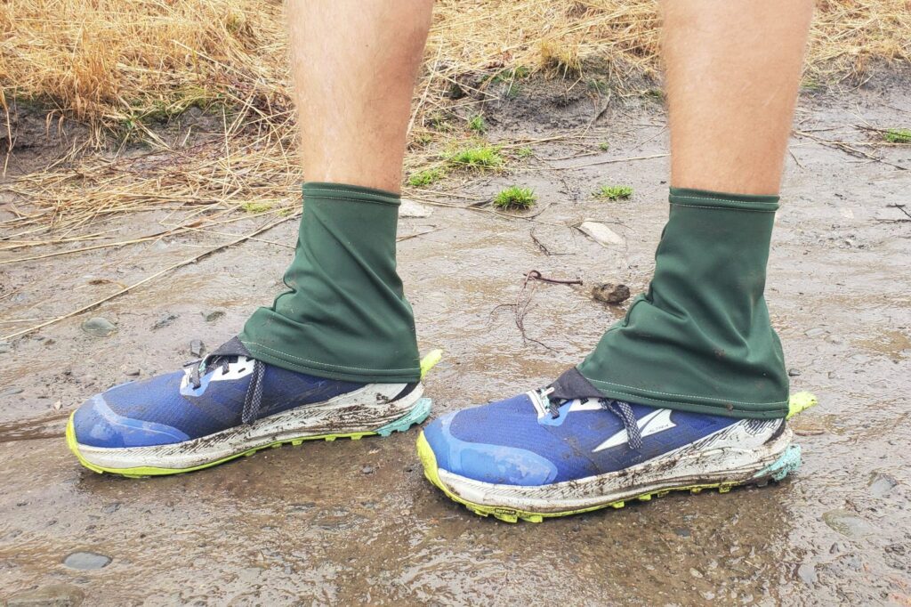 A side shot of green gaiters on a muddy trail.