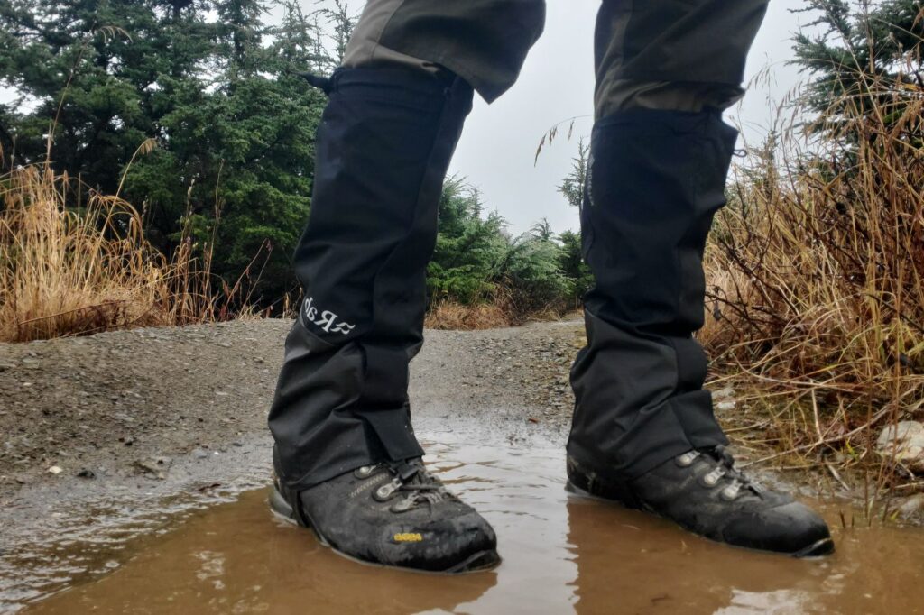 A man stands in a mud puddle showing the weather resistance of hiking gaiters.