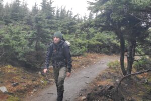 A man hikes though a riany forest wearing a black rain jacket.