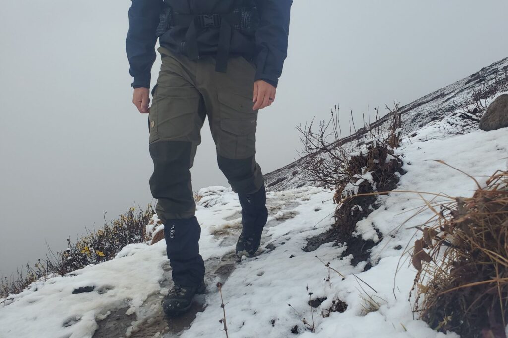 A man hikes up a snowy trail wearing gaiters