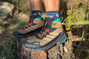 A pair of Adidas Terrex Skychaser AX5 Mid GORE-TEX hiking boots worn outdoors, resting on a tree stump with visible mesh upper and orange laces.