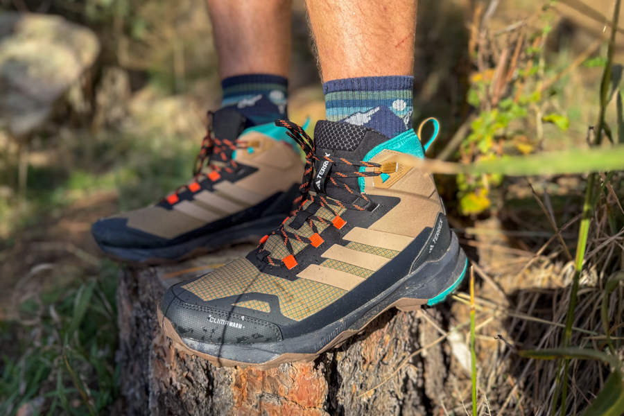 A pair of Adidas Terrex Skychaser AX5 Mid GORE-TEX hiking boots worn outdoors, resting on a tree stump with visible mesh upper and orange laces.