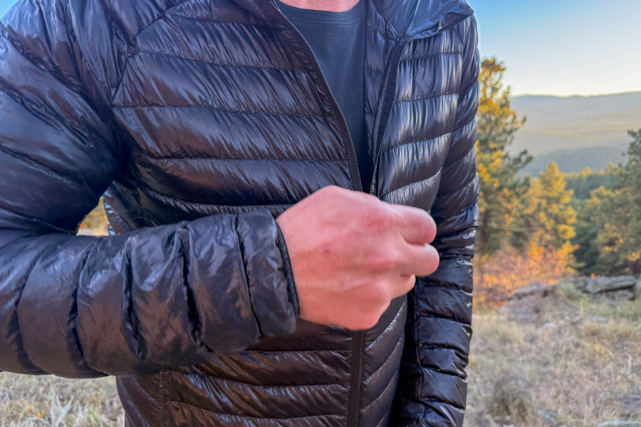 Close-up of the jacket’s front zipper being pulled up, showing the glossy fabric texture and minimalist design.