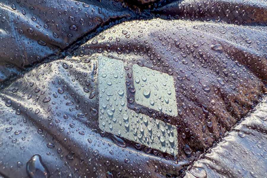 Close-up of the Black Diamond logo on the Deploy Down 0.5 Full Zip Hoody, covered in water droplets demonstrating the jacket’s DWR (durable water repellent) coating.