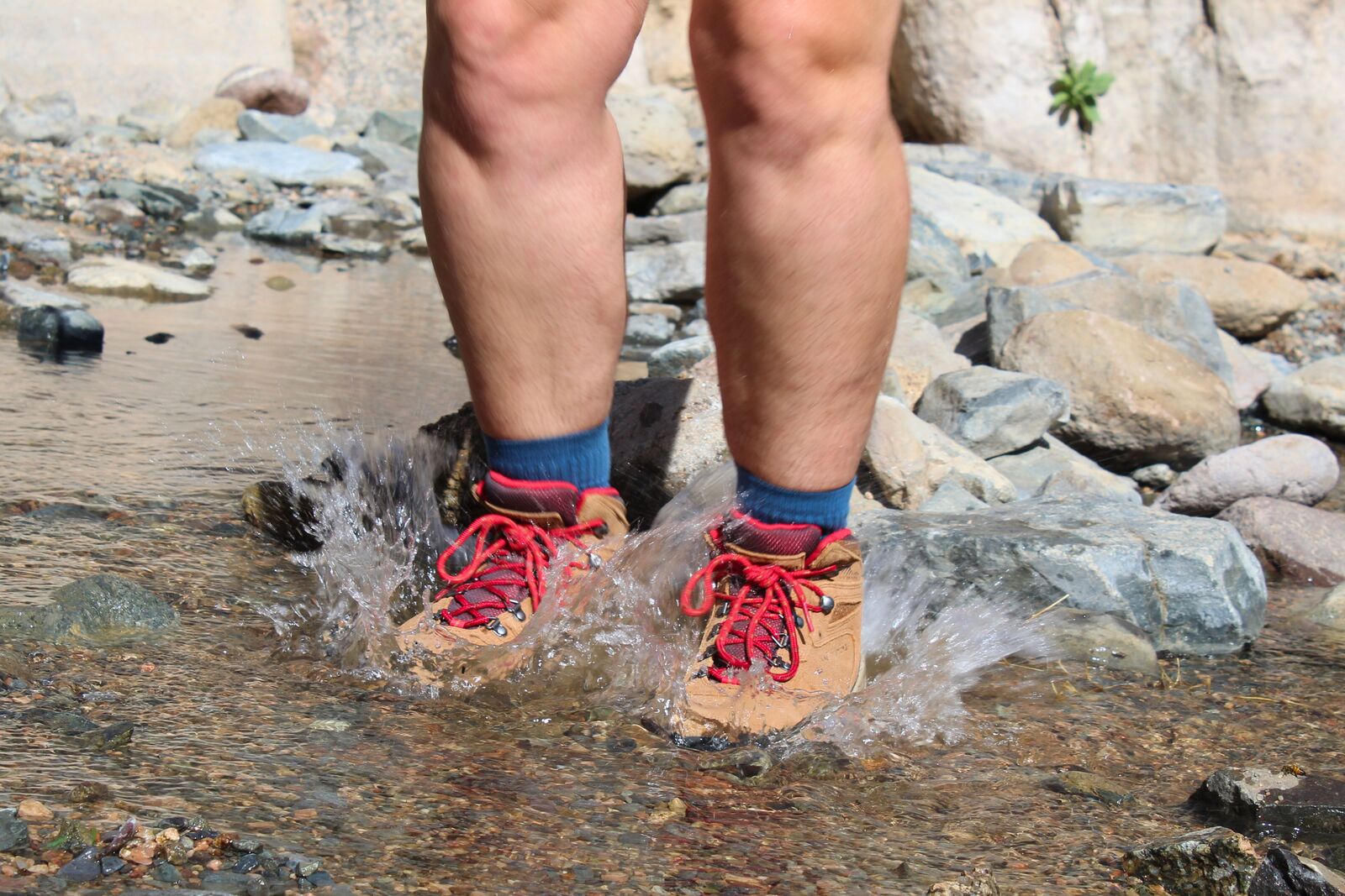 Hiker jumping in a stream wearing the Columbia Newton Ridge Plus Waterproof Amped
