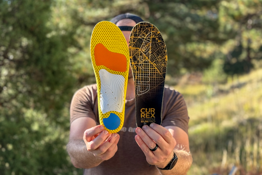 Person holding up both sides of the Currex RunPro insole—top graphic side and colorful underside—outdoors.