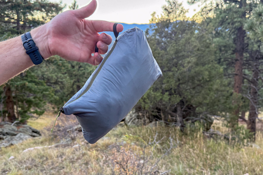 A close-up of a hand holding the Decathlon Simond MT100 Down Jacket packed into its own pocket, demonstrating its compact size and convenient carrying loop.