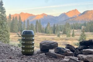 a yellow bear canister sits next to a fire pit with mountains in the background