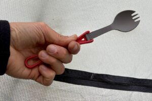 a hand pinches the handle of a plastic folding spork