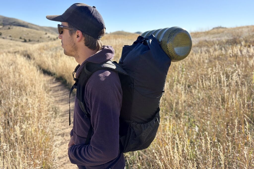 a profile view of a hiker standing with a backpack and a yellow bear canister strapped on top