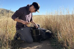 a hiker kneels on a trail while packing food into a bear canister